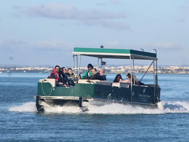 Green tour boat speeding through the water with several passengers on board