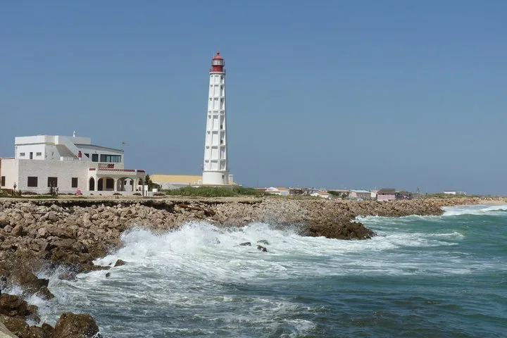 Olas rompiendo contra una costa rocosa con un faro blanco alto