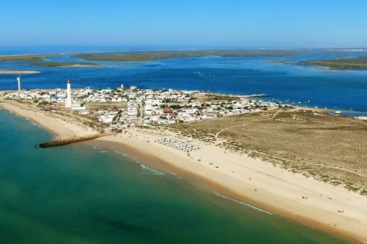 Luftaufnahme einer Küstensiedlung mit einem Leuchtturm auf einer sandigen Halbinsel